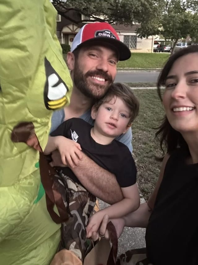 Preston, their son and Laura on Halloween next to a dinosaur costume