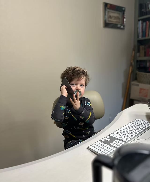 Their son at the office desk, holding a phone to his ear