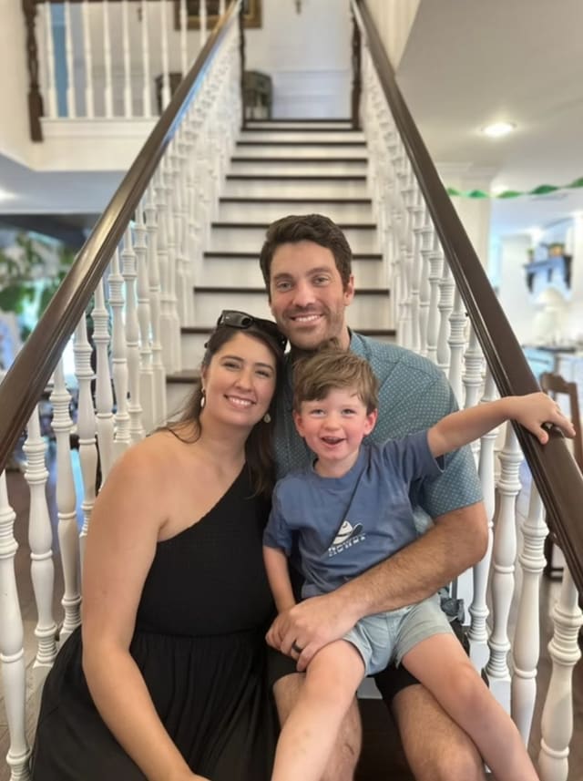 Preston, Laura and their son smiling on a white staircase